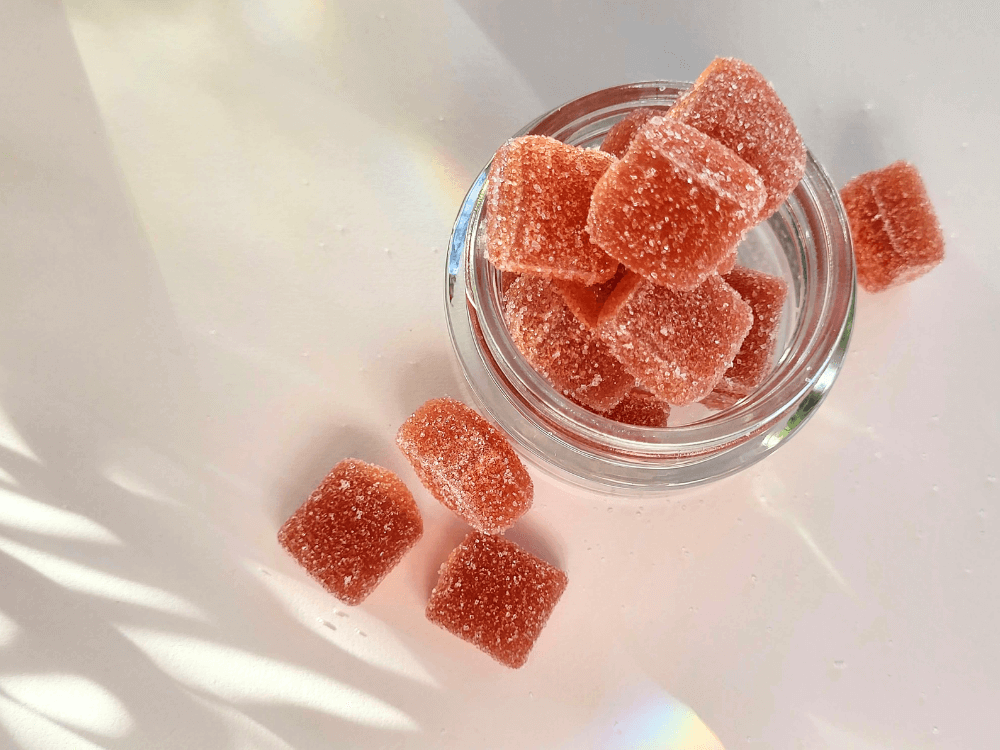 Top view of open jar with orange gummies in jar and beside it.